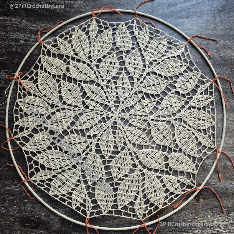 May include: Cream-colored, handmade crochet doily with a floral design, stretched over a circular wooden hoop. The doily is secured with orange thread. The text "@2PIRCrochetbyLara" is visible in the image.