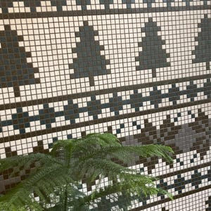 Può includere: Primo piano di una parete rivestita di piccoli riquadri quadrati bianchi, marroni e blu disposti in un motivo geometrico. In primo piano c'è una pianta verde.