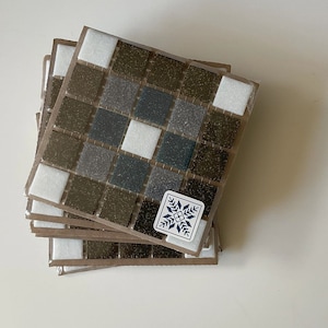 Peut inclure: Un ensemble de dessous-de-verre en mosaïque de carreaux marrons et blancs avec un motif de flocon de neige. Les dessous-de-verre sont en céramique et ont une finition brillante.