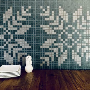 Könnte beinhalten: Eine weiße Keramik-Schneemannfigur mit einer schwarzen Knopfnase und -augen, die auf einer Holzoberfläche vor einer Wand mit einem schwarz-weißen Mosaikfliesenmuster steht.