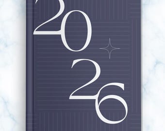 May include: A closed, hardcover notebook with a dark blue cover. The year "2026" is displayed in large, white, elegant font. A four-pointed star is positioned between the numbers. The cover has a subtle geometric pattern.