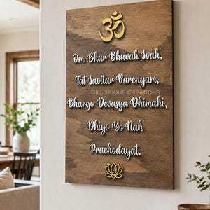 May include: A rectangular wooden wall plaque featuring a gold Om symbol at the top and a gold lotus flower at the bottom. The centre displays the Gayatri Mantra in white raised lettering, reading Om Bhur Bhuvah Svah, Tat Savitur Varenyam, Bhargo Devasya Dhimahi, Dhiyo Yo Nah Prachodayat.