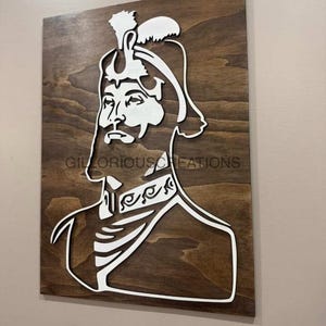 May include: A rectangular wooden wall art piece featuring a dark brown stained plywood background with a white cutout silhouette of a historical figure wearing a feathered cap and military-style uniform. The text GILLORIOUSCREATIONS is visible.