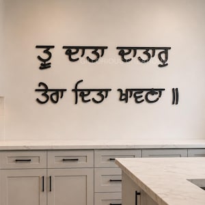 May include: A modern kitchen with light gray cabinets, a stainless steel range, and a white countertop. Black text in a stylized font is mounted on the wall. A small potted plant sits on the countertop.