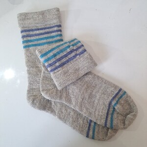 May include: A pair of gray socks with blue and purple stripes. The socks are folded over each other, with the striped portion of the socks visible.