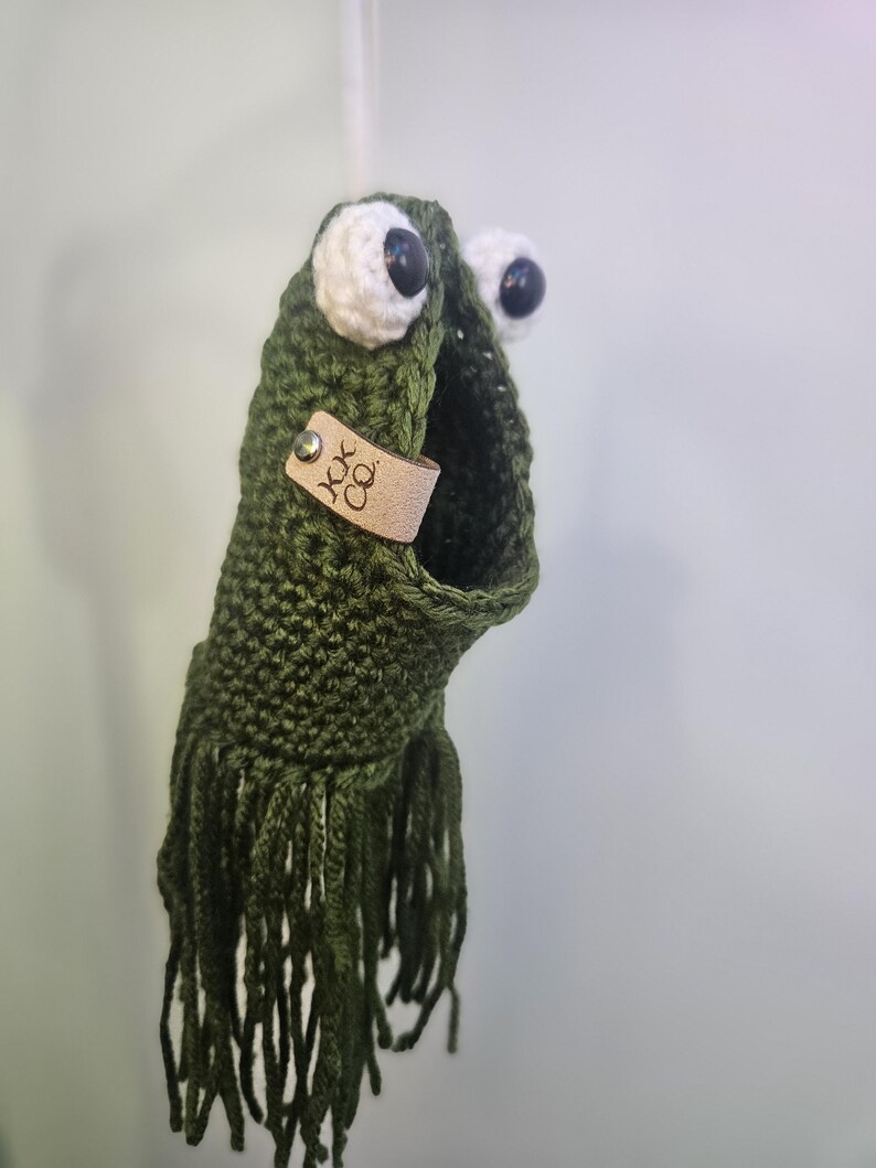 May include: Green crocheted frog with white eyes and black pupils. The frog has a brown leather tag with the text "JOK CO."