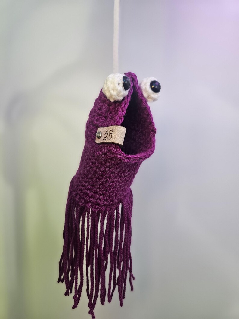 May include: Purple crocheted octopus with white eyes and black pupils. The octopus has a fringe of purple yarn and a small leather tag with the text "XOX CO."