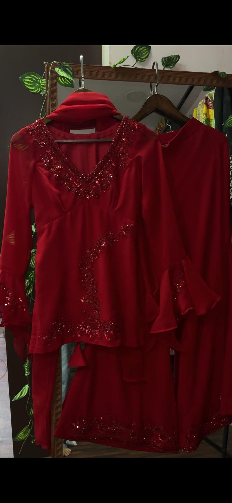 May include: A vibrant red two-piece outfit consisting of a long-sleeved tunic and matching trousers. The tunic features a deep V-neckline, flared sleeves, and intricate red sequin and bead embellishments along the neckline and side panel.
