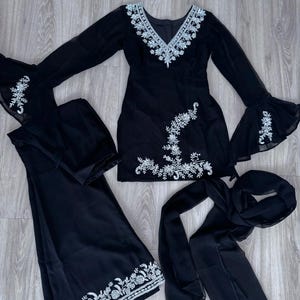 May include: A black three-piece outfit consisting of a long-sleeved tunic with bell sleeves, wide-leg trousers, and a matching scarf. The tunic features a V-neckline and silver floral embroidery, with additional embroidery on the sleeves and hem.