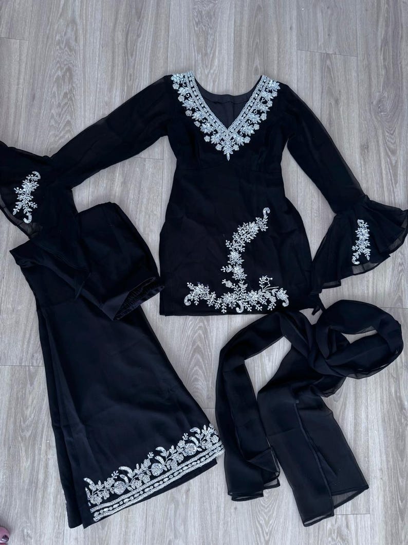 May include: A black three-piece outfit consisting of a long-sleeved tunic with bell sleeves, wide-leg trousers, and a matching scarf. The tunic features a V-neckline and silver floral embroidery, with additional embroidery on the sleeves and hem.