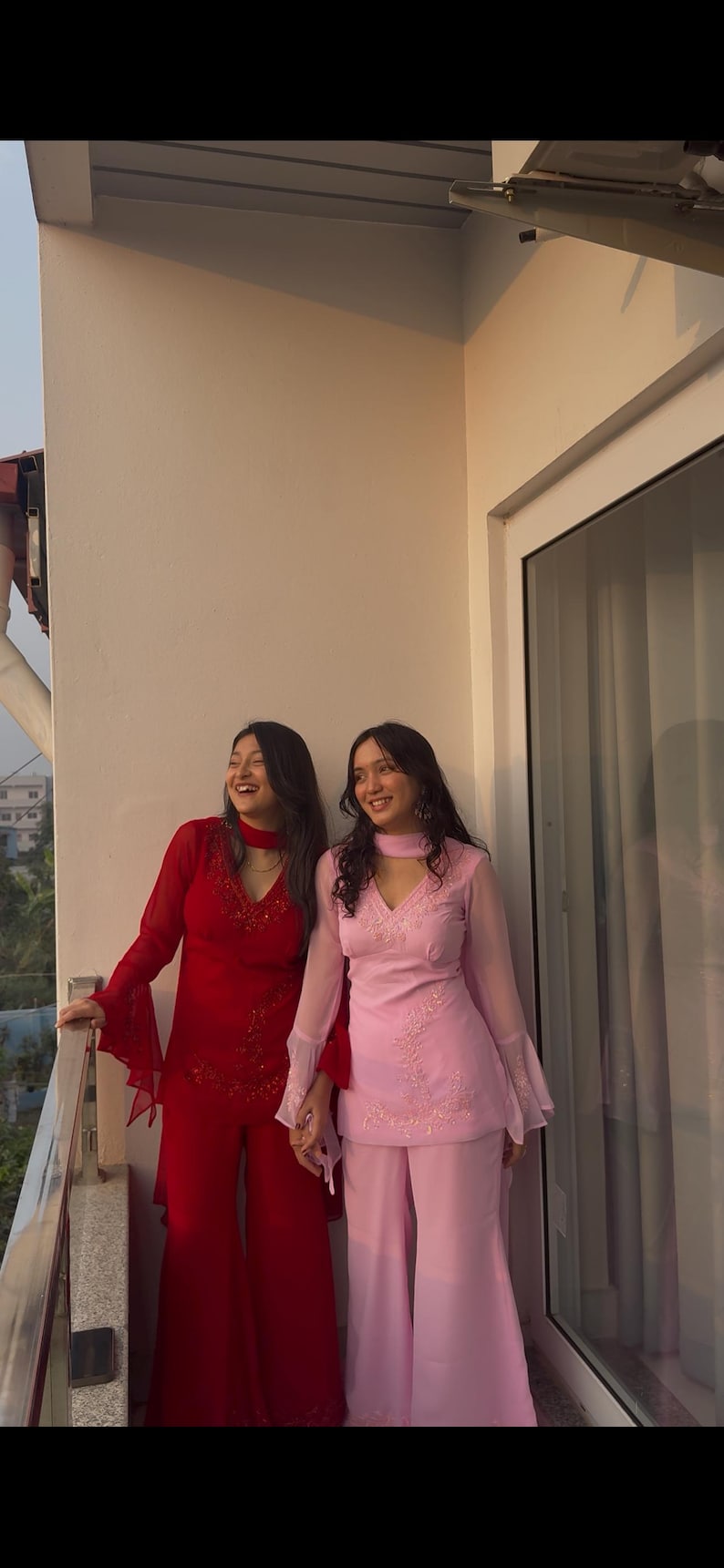 May include: A red long-sleeved tunic with flared sleeves and matching wide-leg trousers, alongside a light pink long-sleeved tunic with flared sleeves and matching wide-leg trousers, both featuring V-necklines and delicate tonal embroidery.