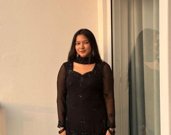 May include: A black long-sleeved tunic featuring a square neckline and intricate beadwork embellishments, paired with matching black wide-leg trousers. The tunic includes a coordinating black fabric neck accessory with matching beadwork details.