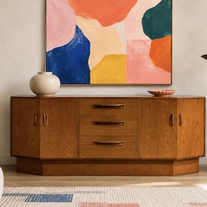 May include: A long wooden sideboard featuring three central drawers with dark handles, flanked by two cabinets with matching handles. The piece has a warm brown finish and a multi-faceted front design, providing a sturdy storage solution.