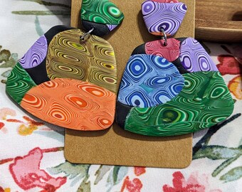 May include: A pair of colorful, abstract patterned earrings. The earrings are made of polymer clay and have a geometric shape. The colors include green, blue, purple, orange, and yellow.