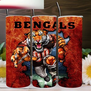 May include: A set of three stainless steel tumblers with a graphic of a tiger football player breaking through a wall. The tumblers are orange and brown with the word "BENGALS" printed in black.