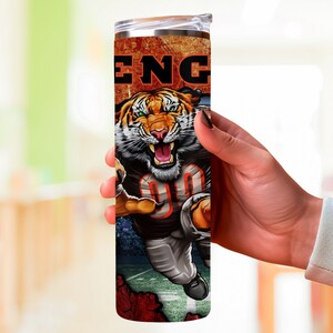 May include: A stainless steel tumbler with a colorful design featuring a tiger wearing a football uniform and the word "ENG" on the side.