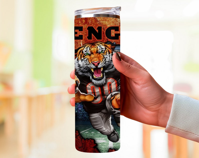 May include: A stainless steel tumbler with a colorful design featuring a tiger wearing a football uniform and the word "ENG" on the side.