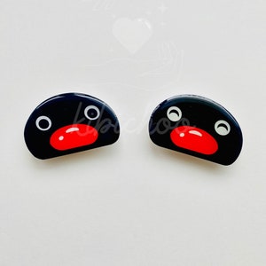 Op de afbeelding: Twee zwarte en witte pinguïn-vormige haarclips van hars met rode snavels.