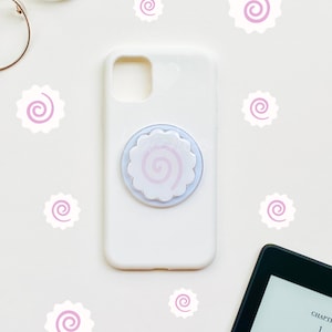 May include: White iPhone case with a pink and white swirl phone grip. The case is surrounded by pink and white swirl stickers.