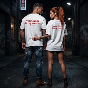 Könnte beinhalten: Zwei weiße T-Shirts mit dem Text "your Mom is my cardio" in Rot. Ein Mann und eine Frau tragen die T-Shirts in einer dunklen Gasse. Der Mann trägt eine blaue Jeans und braune Stiefel. Die Frau trägt schwarze Shorts und braune Stiefel.