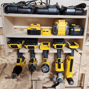 May include: A wooden wall-mounted storage rack with multiple shelves for organizing power tools and batteries. The rack holds six yellow and black cordless drills and several yellow and black batteries.