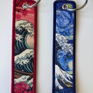 May include: Two rectangular keychains with metal rings. One features a red border and a Japanese wave design with cherry blossoms. The other has a blue border and a starry night wave design.