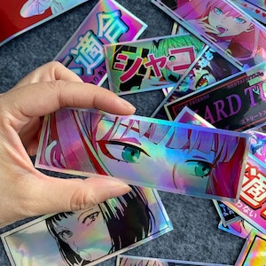 Puede incluir: Una pegatina hologr&aacute;fica con un primer plano del ojo de un personaje de anime con cabello rosa y azul. La pegatina tiene un acabado iridiscente arco&iacute;ris.