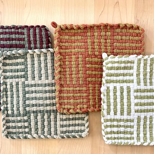 May include: Four woven pot holders in different colors and patterns. The pot holders are square and have a fringed edge. The colors are burgundy, green, orange, and white.