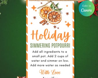 May include: A white rectangular tag with orange detailing, featuring the text "Holiday Simmering Potpourri." The tag includes illustrations of orange slices, cinnamon sticks, and stars. It's tied with twine and decorated with Christmas ornaments.