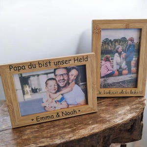 Könnte beinhalten: Zwei Holzbilderrahmen mit Familienfotos. Ein Rahmen hat den Text "Papa du bist unser Held" und "Emma & Noah". Der andere Rahmen hat den Text "Wir haben dich lieb". Die Rahmen stehen auf einer Holzoberfläche.