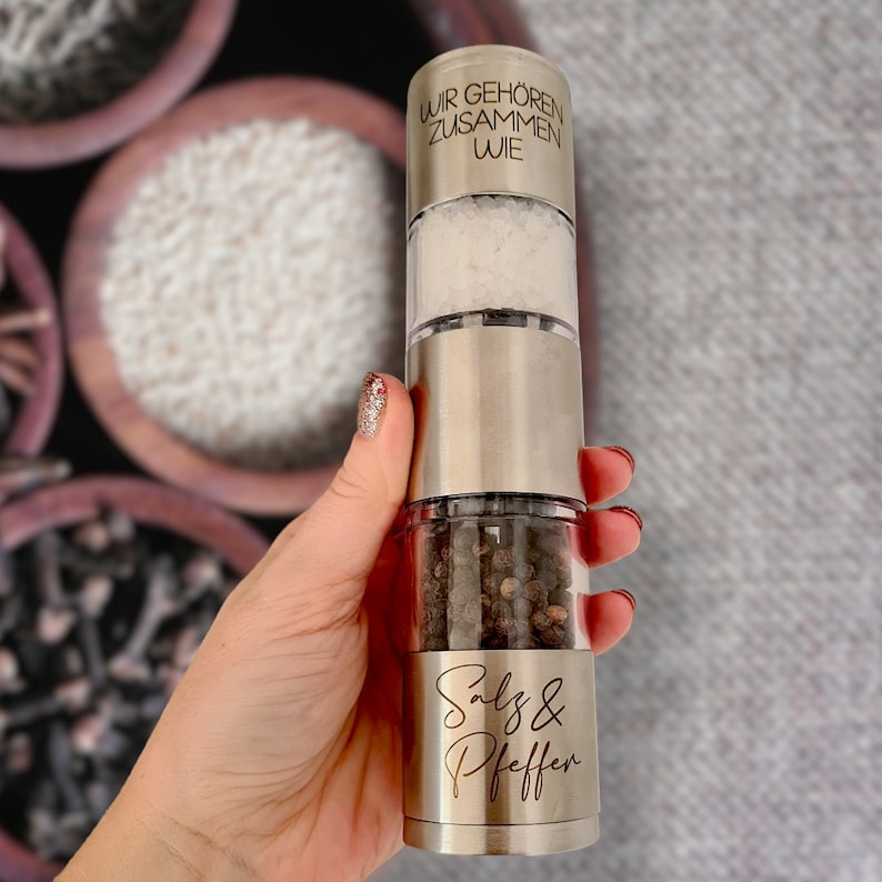 May include: A silver salt and pepper grinder with a clear glass container. The grinder has a label that says "Salz & Pfeffer" and "Wir geh&ouml;ren zusammen wie".
