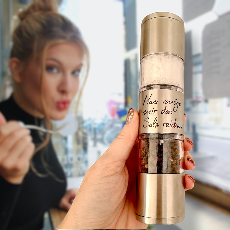 May include: A silver and gold salt and pepper grinder with a handwritten message that says "Man m&ouml;ge mir das Salz reichen".