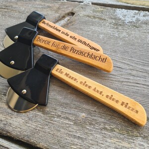 May include: Three black and silver pizza cutters shaped like axes with wooden handles. The handles are engraved with the text "Schneiden wie ein Wikinger", "Bereit f&uuml;r die Pizzaschlacht!" and "Ein Mann, eine Axt, eine Pizza".