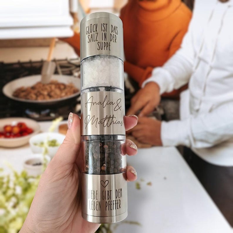 May include: A silver salt and pepper grinder with the text "Gl&uuml;ck ist das Salz in der Suppe" on the top, "Analia & Matthias" on the middle section, and "Liebe gibt dem Leben Pfeffer" on the bottom.