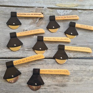 May include: A set of nine wooden pizza cutters with black handles and stainless steel blades. Each cutter has a different engraved saying on the handle. The sayings include "Schneiden wie ein Wikingur", "Bereit f&uuml;r die Pizzaschlacht!" and "Ich bin der Pizzaschlitzer".