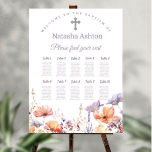 Puede incluir: Un letrero de bienvenida blanco para un bautizo, con el texto "Bienvenida al bautizo de Natasha Ashton. Por favor, encuentra tu asiento." El letrero incluye una cruz y flores de acuarela en naranja, morado y rosa.