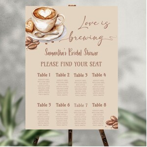 May include: A bridal shower seating plan displayed on an easel. The sign includes a coffee cup with a heart design, the words "Love is brewing," and the name "Samantha." Tables are listed with guest names.