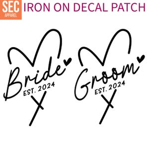 Könnte beinhalten: Zwei Bügelbilder, eines mit dem Wort "Bride" und das andere mit dem Wort "Groom", beide in Herzform mit dem Text "EST. 2024" darunter.