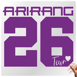May include: A purple graphic with the word "ARIRANG" at the top and the number "26" in a bold, blocky font. Below the number is the word "Tour" with a heart symbol. The background is white.