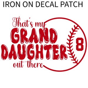 Può includere: Toppa termoadesiva rossa con il testo "That's my Granddaughter out there" e una palla da baseball con il numero 8.