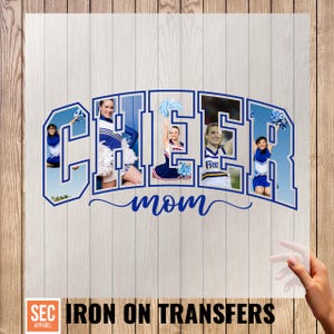 Op de afbeelding: Een blauw-witte opstrijktransfer met het woord "CHEER" en foto's van cheerleaders in de letters, en het woord "mom" eronder. De tekst "SEC APPAREL IRON ON TRANSFERS" staat onderaan.