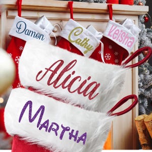 May include: Red Christmas stockings with white faux fur cuffs, personalized with names in various colors. The stockings have red hanging loops and snowflake details, perfect for holiday decor.