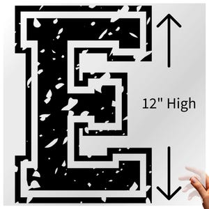 May include: A black and white letter "E" design, 12 inches high, with a distressed, speckled pattern. The letter is outlined in white, with a black interior filled with white speckles. The design is against a white background.