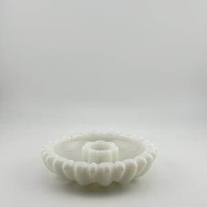 May include: A white, scalloped-edge candle holder with a central, flower-shaped candle cup. The candle holder is made of a solid, opaque material and sits on a white surface. The design is simple and elegant.