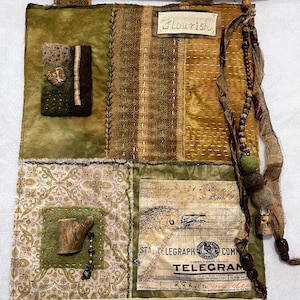 May include: Textile wall hanging with a wooden dowel and a cream-colored fringe. The artwork features various fabrics in shades of green, brown, and gold, with decorative stitching and embellishments. The word "Flourish" is written on a small tag.