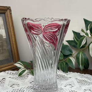 May include: A clear glass vase with a flared top and a textured, swirling design. The vase has a decorative red floral design inside. The vase is approximately 25 cm tall.