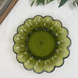 Peut inclure: Un plat à œufs en verre vert avec une surface texturée. Le plat comporte 12 compartiments individuels pour contenir des œufs.