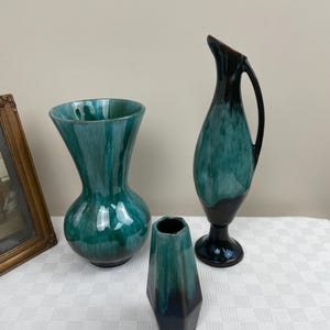 Peut inclure: Trois vases en céramique dans des tons de vert et de brun. Le plus grand vase est un vase rond à large ouverture avec un bord évasé. Le vase de taille moyenne est un vase haut et fin avec une ouverture étroite. Le plus petit vase est un vase court et trapu de forme hexagonale.