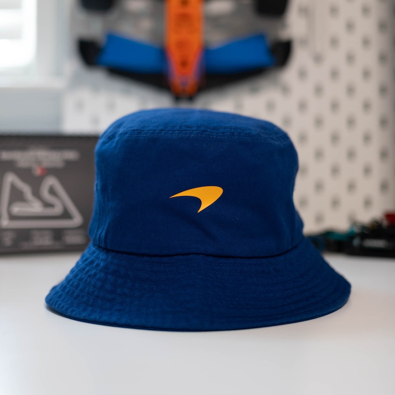 May include: A blue bucket hat with a yellow McLaren logo embroidered on the front.