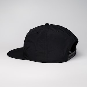 May include: A black, flat-brimmed baseball cap with a black adjustable strap in the back.